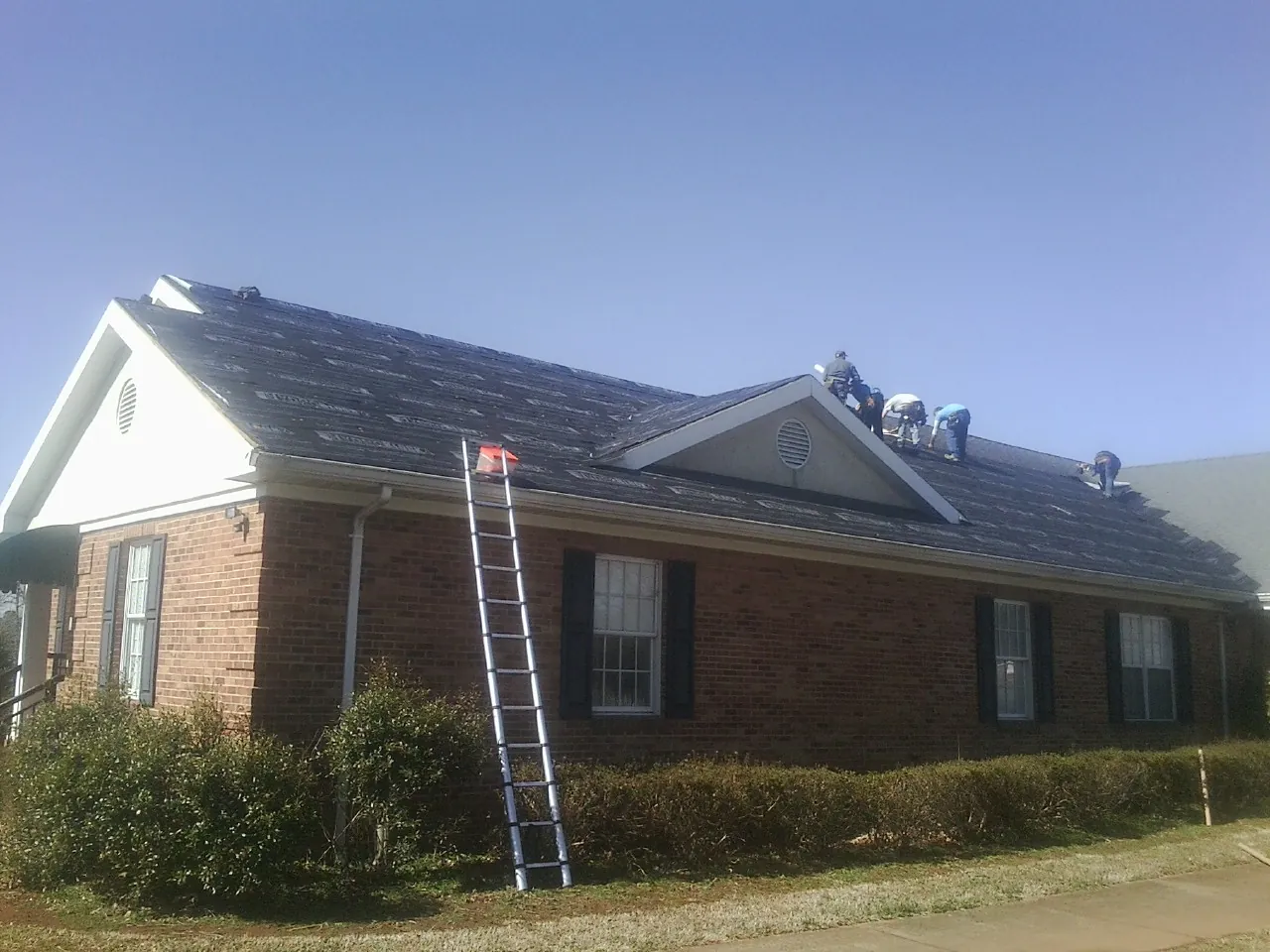Crew tearing shingles off a brick ranch roof with a ladder set — Emergency Roof Repair work by our crew in Bolivar