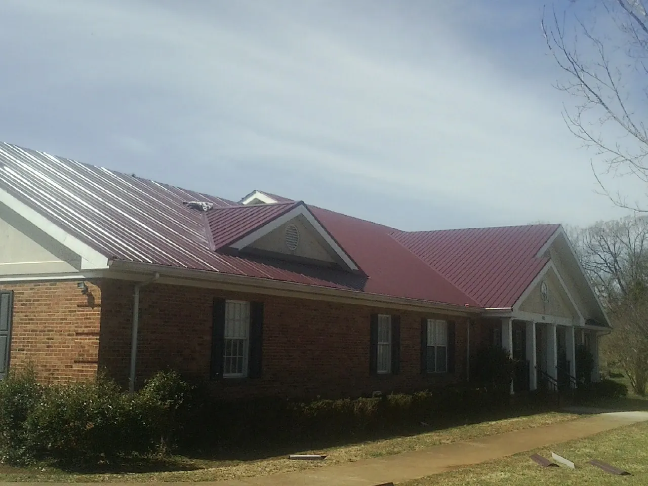 Red metal roof with gabled entries on a long brick building, from a Hail Damage Roof Repair job in Bolivar