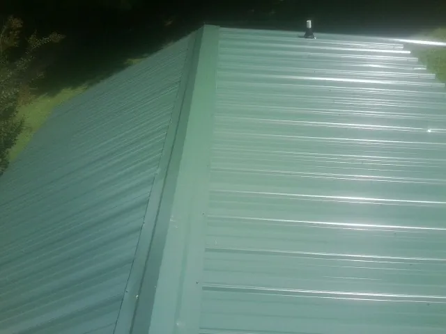 New green metal panels meeting at the ridge of a roof — Flat Roof Repair work by our crew in Bolivar